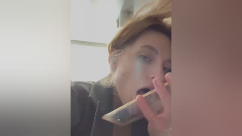 Media: Video of a woman with blonde hair, wearing a black jacket, looking through a window, holding a phone to her ear.