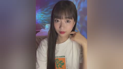 Media: Video of an East Asian woman with straight black hair, wearing a white t-shirt with a green dragon logo, and red lipstick, against a blurred, colorful background.