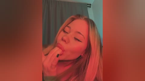 Media: A video of a young woman with long blonde hair and fair skin, wearing black nail polish, licking her fingers, set against a red-tinted background.