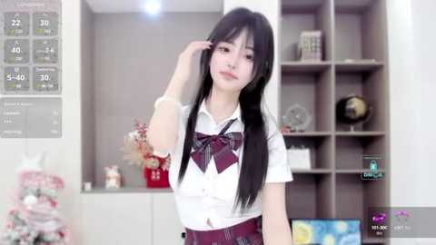 Media: A video of an Asian woman with long black hair in a white blouse and maroon tie, posing in a modern, minimalist living room with grey shelving.