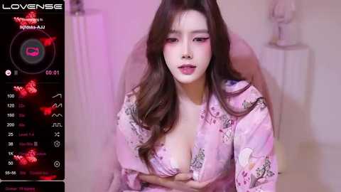 Media: A video of an East Asian woman with long brown hair, wearing a pink floral kimono, revealing cleavage, in a dimly lit room, with a live stream overlay.