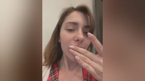 Media: A video shows a young woman with light skin, straight brown hair, and wearing a red plaid shirt. She's licking her finger and has a soft, slightly blurred background.