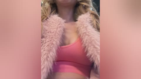 Media: Video of a woman with long blonde hair, wearing a pink ribbed sports bra and fluffy pink shawl, blurred background.