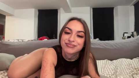 Media: Video of a smiling, light-skinned woman with long brown hair, lying on a gray couch in a modern, minimalist living room.