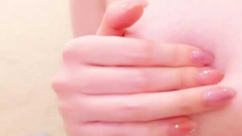 Media: Close-up video of a Caucasian hand with neatly manicured nails, lightly tanned skin, gently pressing against a soft, light pink surface. The background is out of focus, suggesting a smooth, possibly fabric texture.