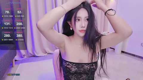 Media: Video of an Asian woman with long black hair, wearing a black lace dress, adjusting her hair in a modern, brightly-lit room with white curtains.