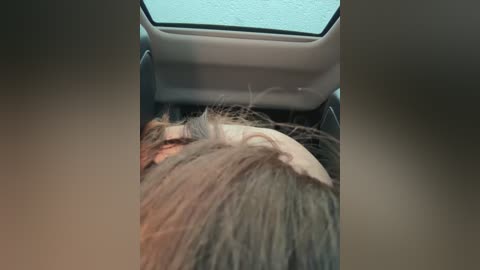 Media: Video of a person with short, light brown hair, lying on their back inside a car with a visible sunroof. The person appears to be sleeping, with their head partially visible. The car's interior is light-colored and modern.