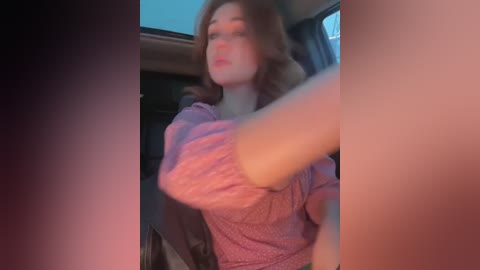 Media: A blurry video of a woman with fair skin and wavy brown hair, wearing a pink blouse, driving a car at night. The background shows dimly lit car interior and outside night sky.