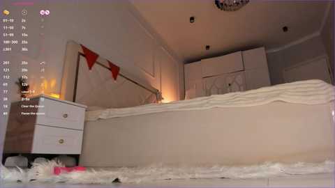 Media: Video of a dimly lit, cozy bedroom with a large bed, white dresser, and decorative red pennant banner. The room has a soft, intimate ambiance with warm lighting.