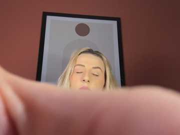 Media: A video of a blonde woman with closed eyes and relaxed expression in a bathroom mirror, framed by a black frame, with a red wall background.