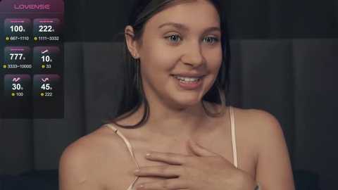 Media: Video of a smiling woman with light skin and brown hair, wearing a light-colored tank top, against a dark, blurry background. Game UI with stats visible.