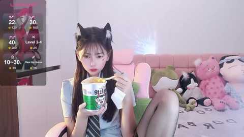 Media: Video of a young Asian woman with long black hair and cat ears, sitting on a pink bed, eating ramen, surrounded by plush toys.