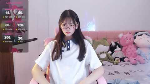 Media: A video of an East Asian woman with long black hair, glasses, and a white shirt sitting on a bed adorned with stuffed animals.