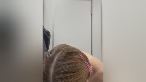 Media: A video of a person with light brown hair, wearing a pink headband, leaning against a white bathroom door, with a towel hanging on the left.