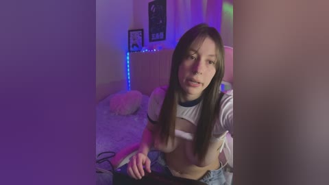 Media: A video of an Asian woman with long, straight black hair, wearing a cropped white top, taking a selfie in a dimly lit room with purple LED strip lighting, plush toys, and framed art on the wall.