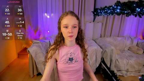 Media: Video of a young, fair-skinned girl with curly brown hair, wearing a pink tank top, in a cozy living room with festive decorations.