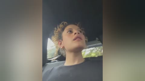 Media: A video of a young person with curly hair, wearing a dark shirt, looking out a car window at a green, blurred background.