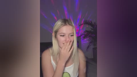 Media: A video of a blonde, fair-skinned woman with straight hair, wearing a white tank top, covering her mouth with her hand, under purple and pink neon lights.