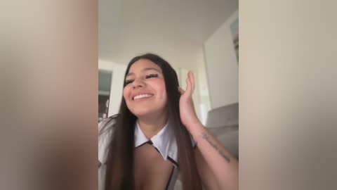 Media: A video of a young, smiling Asian woman with long black hair, wearing a white collared shirt, captured from a low angle.