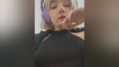 Media: A video of a young woman with pale skin and short blonde hair, wearing purple headphones, adjusting a black top.