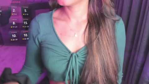 Media: Video of a woman with long, wavy brown hair, wearing a green ribbed crop top, against a purple-lit background, displaying a fitness app screen.