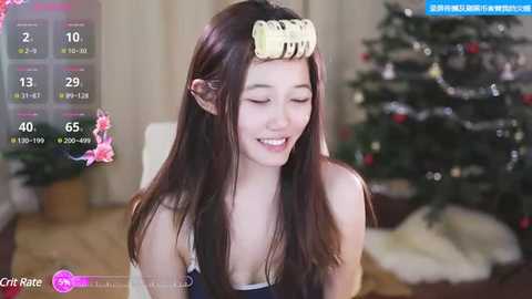 Media: Video of a smiling Asian woman with long dark hair, wearing a yellow hairpiece, sitting in a living room with a decorated Christmas tree in the background.