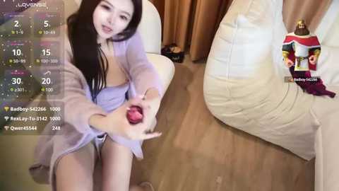 Media: Video of an Asian woman with long black hair, wearing a sheer robe, holding a red dildo, seated on a beige couch, with a TV showing a dating profile.