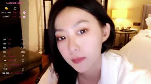 Media: A video of an East Asian woman with straight black hair and fair skin, wearing a white top, taken indoors with a warm yellow light in the background.