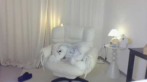 Media: Video of a plush white armchair with a stuffed animal, a white table lamp, and a white curtain backdrop, creating a cozy, whimsical ambiance.