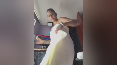 Media: A video of a pregnant woman in a white dress, mid-kick, inside a dimly lit room with purple walls and cluttered shelves.