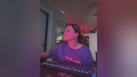 Media: Video of a young woman with dark hair, wearing a purple shirt, typing on a computer keyboard in a dimly lit room with red LED lighting.