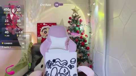 Media: Video of a cozy, Christmas-decorated living room with a pink gaming chair, a decorated Christmas tree, and a framed picture of Santa Claus.