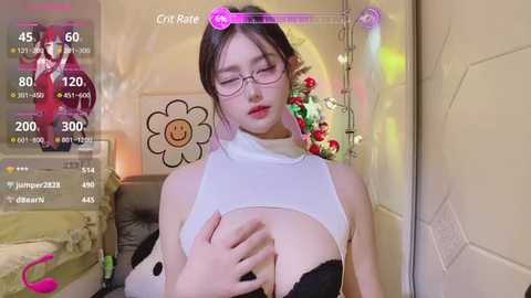 Media: Video of a young Asian woman with glasses, fair skin, and large breasts, wearing a revealing white top, in a cozy bedroom with a pink unicorn lamp and floral decor.