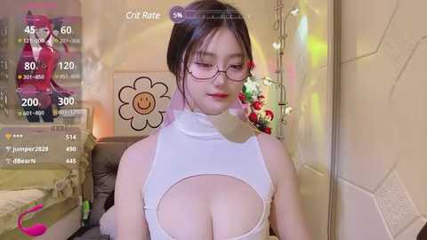 Media: Video of an East Asian woman with glasses, large breasts, wearing a revealing white top, in a colorful bedroom with a flower wall decal and gaming display.