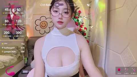 Media: A video of a young Asian woman with fair skin, glasses, and a high-cut, white crop top revealing ample cleavage, in a cozy, festive bedroom.