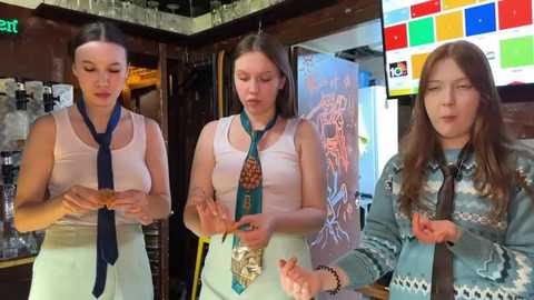 Media: Video of three women, two with long brown hair, one with glasses, in casual attire, holding cards, in a bar with colorful digital screens, bar counter, and glasses.