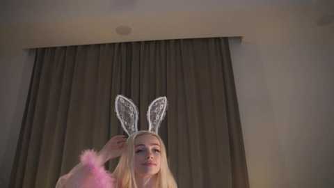 Media: Video of a blonde woman in bunny ears, adjusting them, against a dark curtain background.