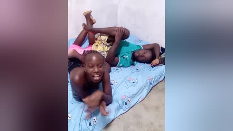 Media: Video of two African children, one lying on a blue bedsheet with cartoon characters, the other sitting on the bed, both smiling.