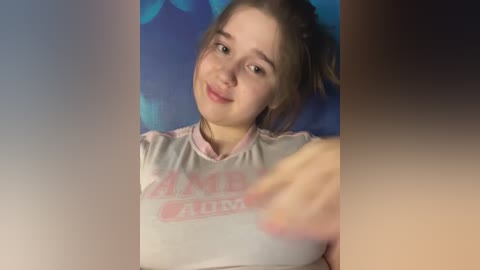 Media: A video of a young Caucasian girl with fair skin and light brown hair in pigtails, wearing a light pink sports top with \"AMIE FLEMING\" in pink text, against a blue background.