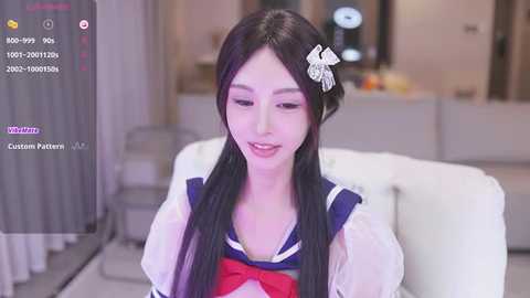 Media: Video of a young Asian woman with long black hair, wearing a sailor schoolgirl outfit, seated on a white couch in a modern living room.