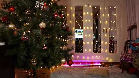 Media: Video of a cozy living room with a decorated Christmas tree adorned with gold and red ornaments, fairy lights, and a TV visible through glass doors.