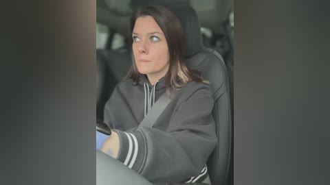 Media: A video of a woman with long brown hair in a gray jacket, driving in a car with a blurred background.