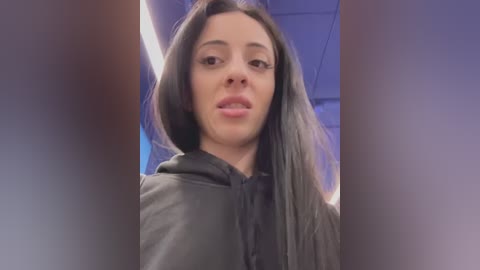 Video of a young woman with long, straight black hair, wearing a black smock, in a salon setting with fluorescent lighting and blue accents.