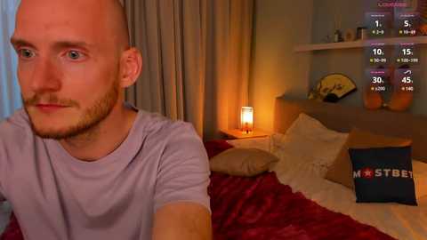 Media: Video of a man in a lavender t-shirt, sitting on a bed with red and white bedding, watching a \"Most Streamed\" app on a TV, in a cozy bedroom with a warm glow.