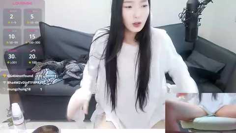 Media: Video of an East Asian woman with long black hair, wearing a white long-sleeve shirt, seated on a black sofa with a checkered blanket.