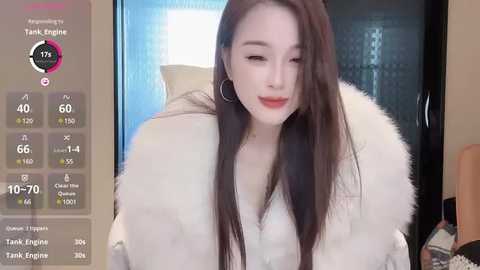 Media: A video of an East Asian woman with long, straight brown hair and fair skin, wearing a white fur coat, in a modern, brightly-lit room.