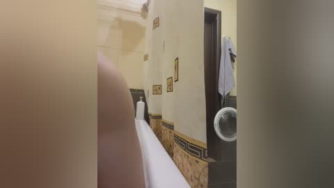 Media: Video of a bathroom with a beige-tiled wall and a white sink, featuring framed artwork and a white towel hanging on a door knob.