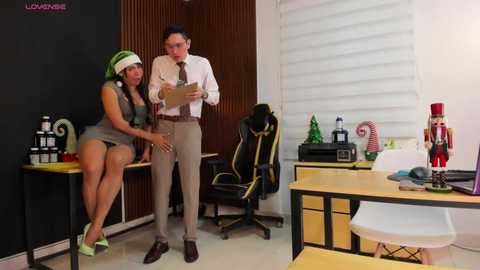 Media: Video: A young, curvy woman with dark skin in a green headband and shorts, and a man in a white shirt and tie, stand in a modern office.