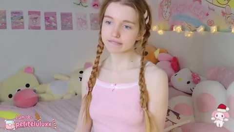 Media: A video of a young Caucasian woman with light skin and long blonde braids, wearing a pink tank top, standing in a pastel-themed room filled with plush toys and fairy lights.