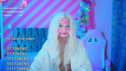 Media: A video of a young woman with long, platinum blonde hair, wearing a white bathrobe, sitting in a room with neon pink and blue striped wallpaper. Text overlays her face with TikTok statistics.